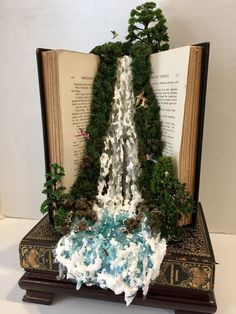 an open book with miniature waterfall and trees on it's cover, sitting on a table