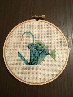 a cross stitch fish is hanging on a wooden hoop with thread in it's center