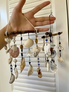 a hand is holding a wind chime with seashells hanging from it