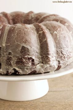 a bundt cake sitting on top of a white cake plate covered in frosting