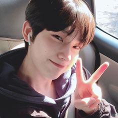 a young man sitting in a car making the peace sign with his hand and wearing a hoodie