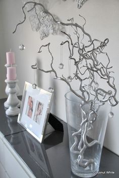 a vase with some branches in it next to a picture frame and candlesticks