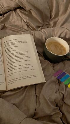 an open book sitting on top of a bed next to a cup of coffee