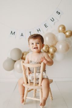 a baby sitting in a wooden high chair with balloons behind it and the words mathieus on the wall