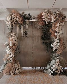 an arrangement of flowers and greenery in front of a concrete wall for a wedding ceremony