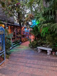 a brick walkway with benches and trees in the background at night, surrounded by greenery