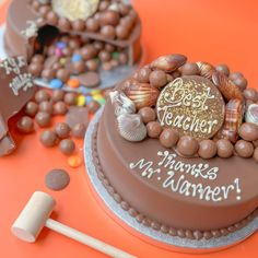 two cakes decorated with seashells and candy on an orange tablecloth, one is for teachers