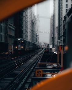 a train traveling down tracks through a city next to tall buildings on a cloudy day