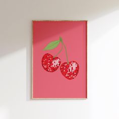 two cherries on a pink background in a wooden frame hanging on a white wall