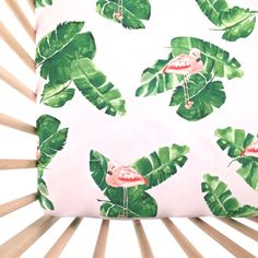 a pink flamingo pillow sitting on top of a wooden crib next to green leaves