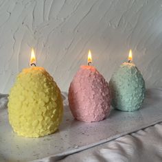 three small candles sitting on top of a white table next to an egg shaped candle holder