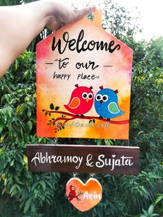 a hand holding a sign with two birds on it that says welcome to our happy place