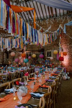 This image shows a dining area at a colourful barn wedding. This image shows rows of dining tables, with bright orange table runners, tableware, orange and white napkins, brass candlesticks, candle holders and disco balls. Above the tables are strings of colourful streamers and round paper lanterns. Vintage Style Wedding Decor, Firehall Wedding Reception, Festival Wedding Ideas, Wedding Streamers, Funky Wedding, Wedding Dining, Tops Winter, Female Jacket