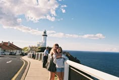 two women hugging each other while standing on the side of a road by the ocean