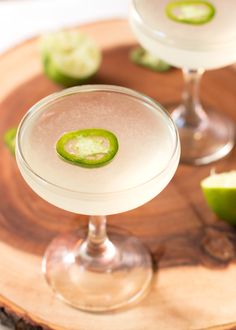 two margaritas sitting on top of a wooden tray with lime slices around the rim