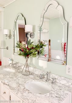 a bathroom with marble counter tops and two mirrors on the wall above it is decorated with greenery