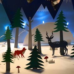 paper cut out of trees and deer in the snow with lights on them, surrounded by mountains