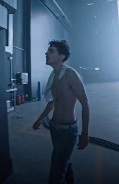 a shirtless man is walking in an empty parking garage with his hand on his hip