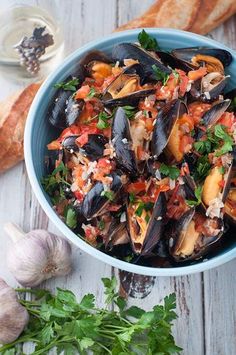 a blue bowl filled with mussels and garnished with parsley next to bread