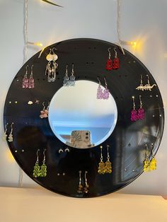 a black plate with earrings hanging from it's sides and a mirror in the middle