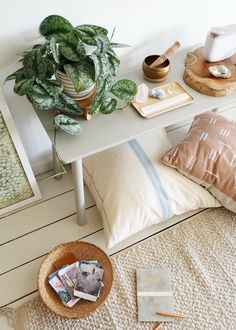 a white table topped with lots of books and pillows next to a potted plant