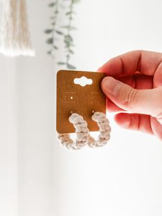 a person holding up a small card with two white beads on it and a plant in the background