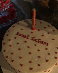 a heart shaped cake with the words sweet sixteen written on it and two candles in the shape of hearts