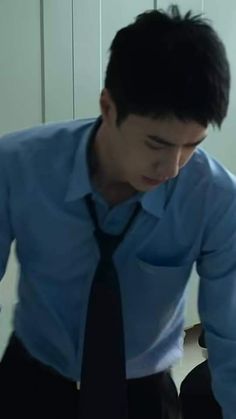 a man wearing a blue shirt and black tie looking down at his cell phone while sitting on a chair