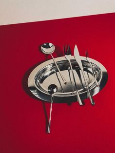 there are forks, spoons and knives in the bowl on the red tablecloth