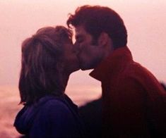 a man and woman kissing in front of the ocean