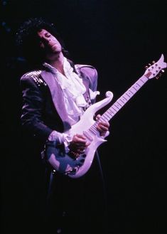 a man with an electric guitar in his hand and wearing a purple suit on stage