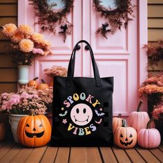 a black tote bag sitting on top of a wooden table next to pumpkins