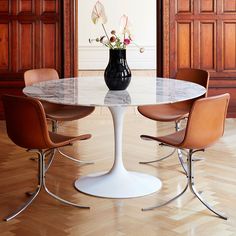 an oval marble table with four chairs around it and a black vase on the top