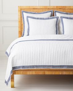 a bed with white and blue bedspread on top of wooden headboard next to wall