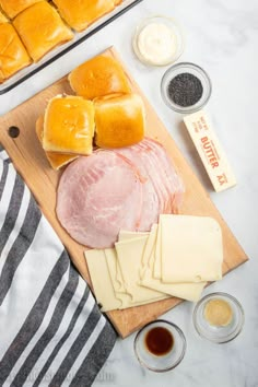 ham, cheese and other ingredients laid out on a cutting board next to bread rolls