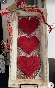 two red hearts are in a frame with ribbon on the top and one is made out of wood