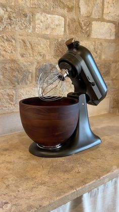 a wooden bowl with a whisk in it on top of a counter next to a stone wall