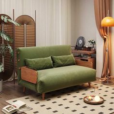 a green couch sitting on top of a wooden floor next to a table and lamp