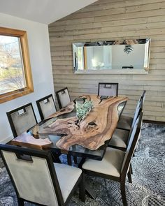 a dining room table with chairs and a mirror on the wall above it, in front of a window