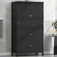 a tall black cabinet with two drawers in the corner and a vase on top of it