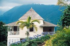 a white house with blue flowers in front of it and mountains in the back ground