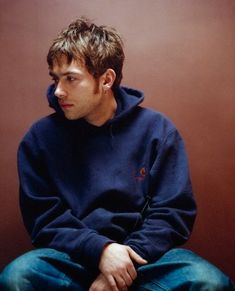 a young man sitting on top of a wooden floor wearing a blue sweatshirt and jeans