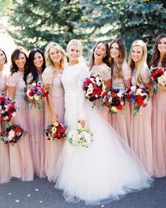 a group of women standing next to each other wearing dresses and holding bouquets in their hands