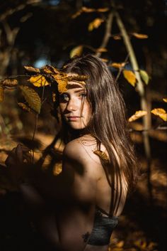 a woman with long hair is posing for a photo in the woods surrounded by leaves