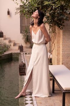 a woman in a long white dress standing next to a pool and looking up at the sky