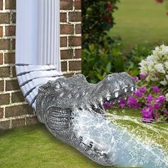 an alligator statue sitting on top of a lush green field next to purple and white flowers