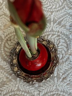 a red vase sitting on top of a white tablecloth covered table with a flower in it