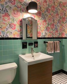 a bathroom with floral wallpaper and green tiles on the walls, along with a white toilet and sink