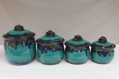 four ceramic jars with lids are sitting on a white tableclothed surface, one is blue and the other is green