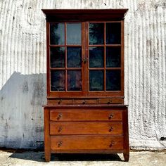 an old wooden dresser sitting in front of a white wall with glass doors on it